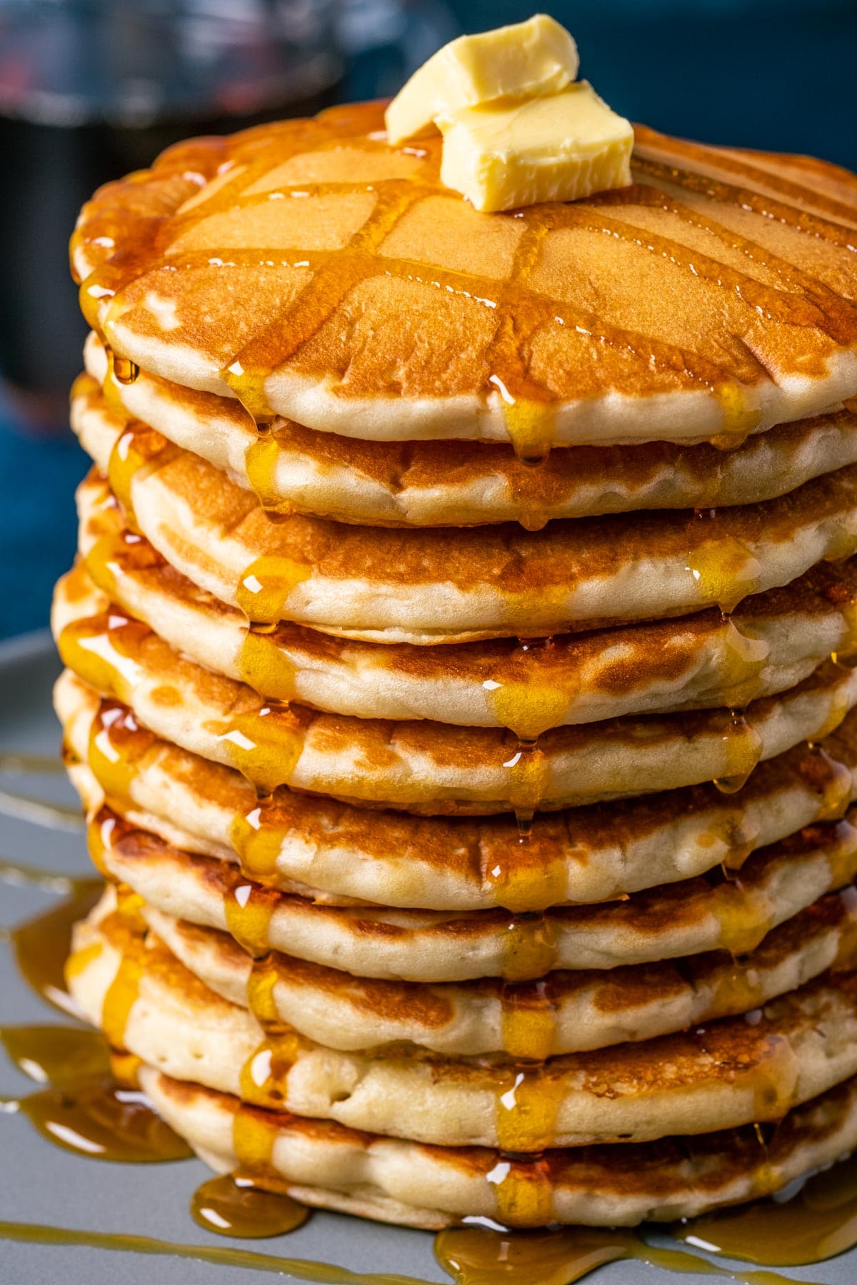 Stack of vegan buttermilk pancakes topped with vegan butter and syrup on a blue plate. 