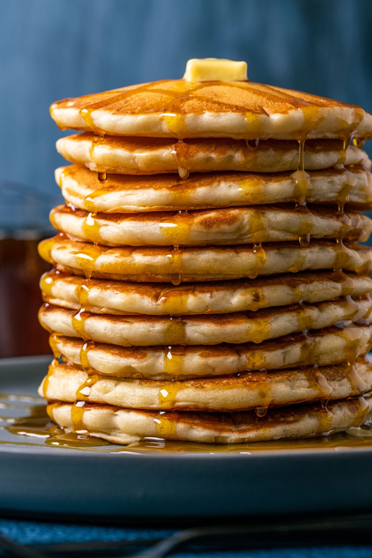 Stack of vegan buttermilk pancakes topped with vegan butter and syrup on a blue plate.