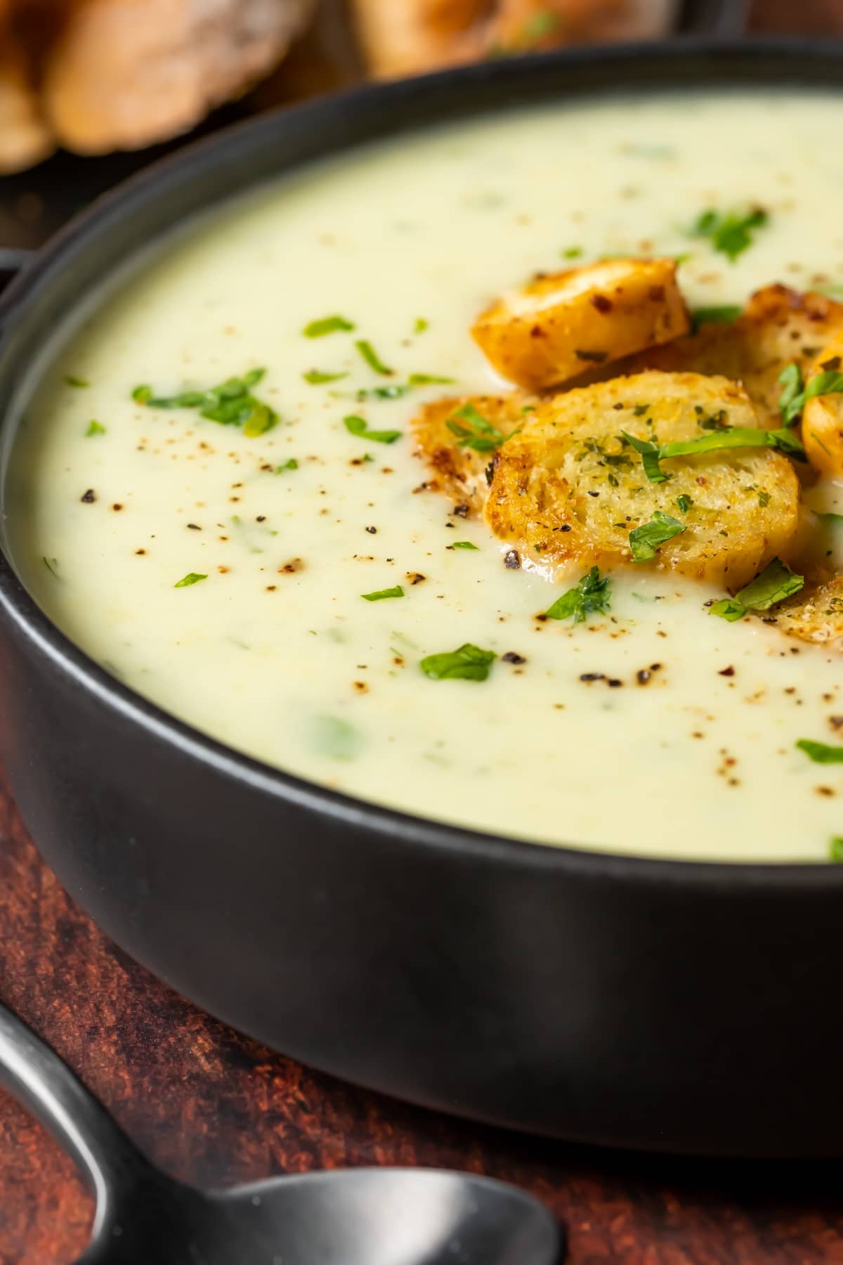 Vegan celery soup with black pepper, parsley and croutons in a black bowl.