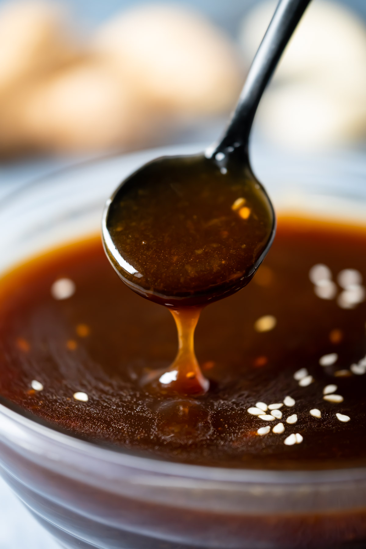 Vegan teriyaki sauce topped with sesame seeds in a glass dish with a spoon.